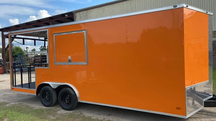 Orange food trailer with black wheels and a serving window, parked outside.