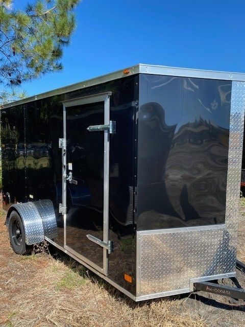 Black enclosed cargo trailer with diamond plate accents, parked outdoors.