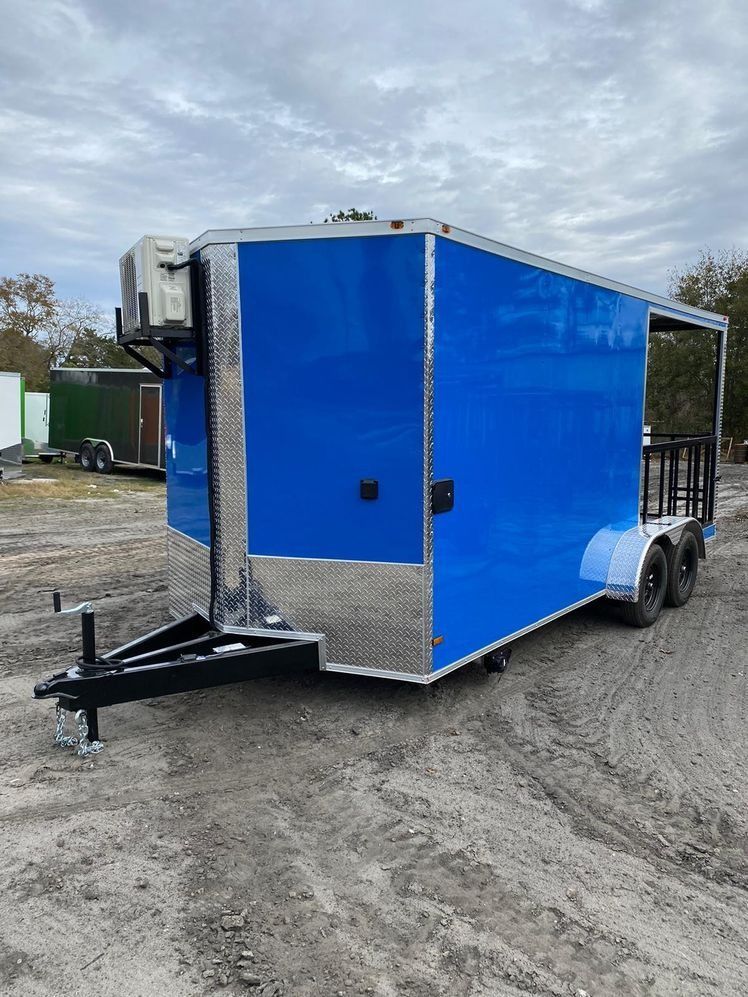 Blue food trailer with air conditioning unit, on a gravel lot under a cloudy sky.