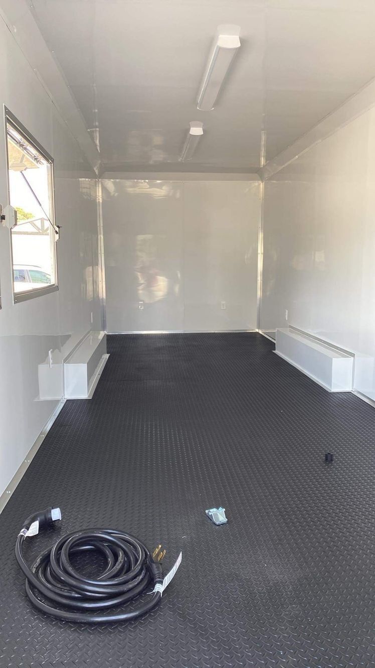 Interior of an empty white utility trailer with black flooring, a window, and a coiled black cable on the floor.