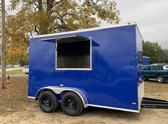 Blue food trailer with a large serving window, parked outdoors.