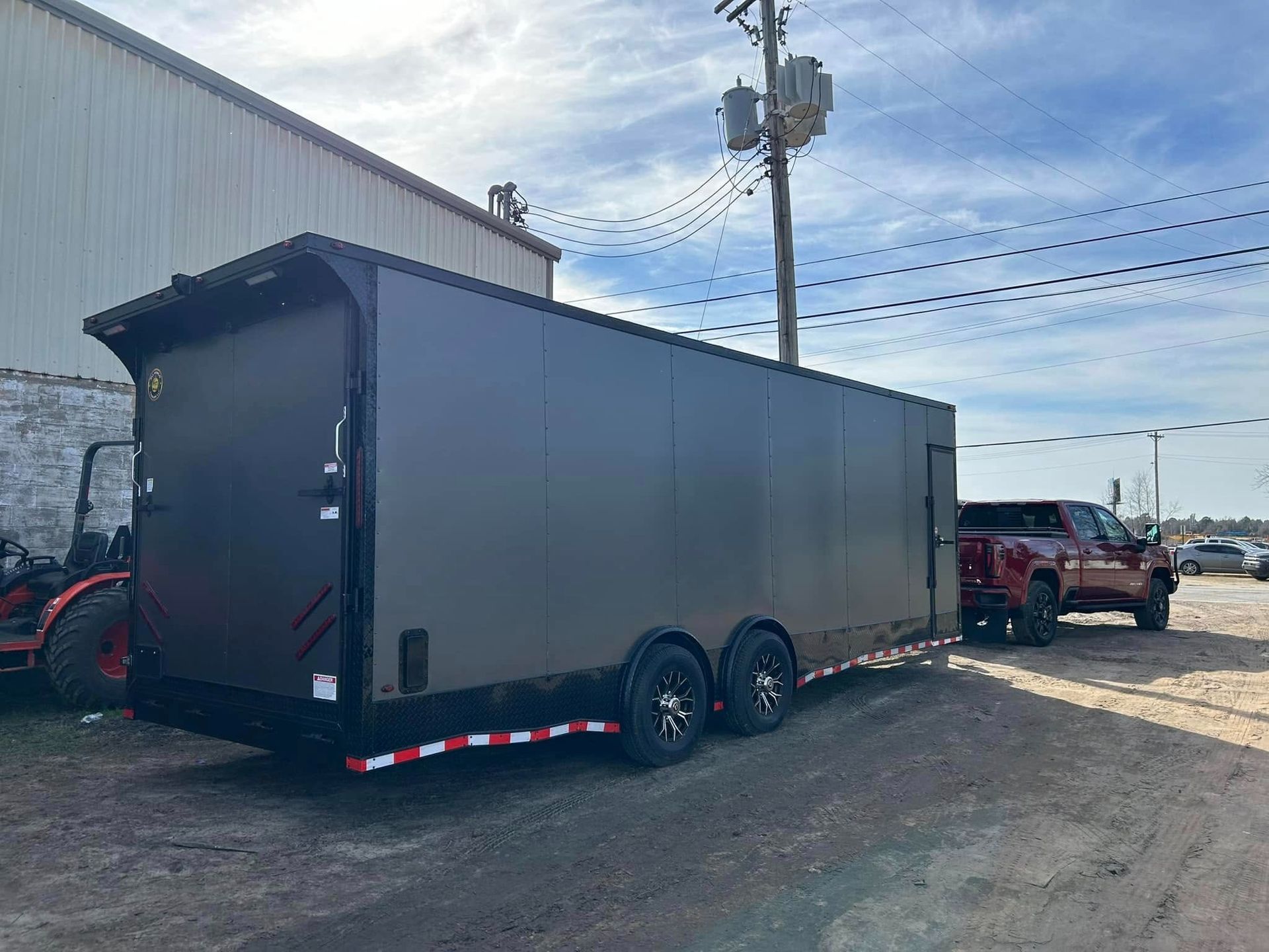 Dark gray enclosed trailer hitched to a truck, parked outside a building on a sunny day.