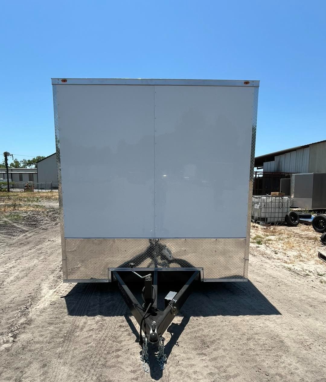 A white enclosed trailer with a black hitch, parked outside.