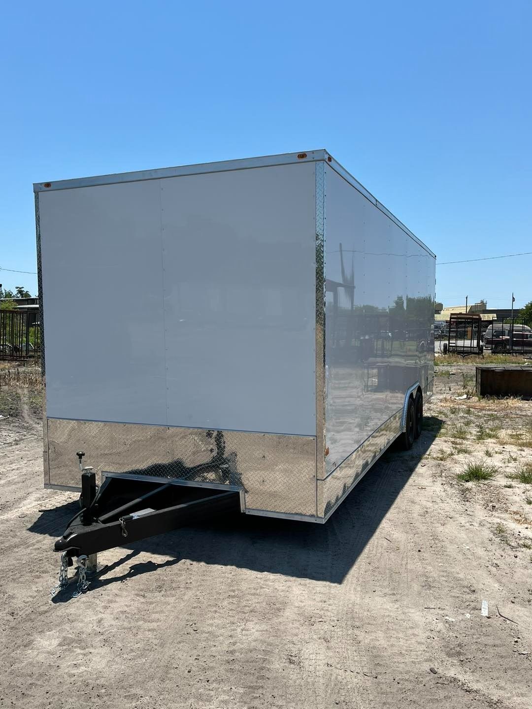 White enclosed trailer on a gravel lot under a clear blue sky.