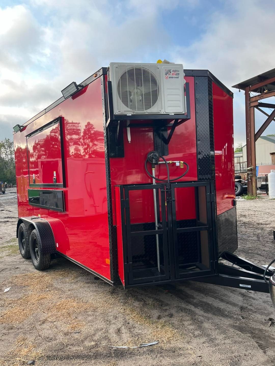 Red food trailer with black accents, air conditioning unit, and open serving window outdoors.