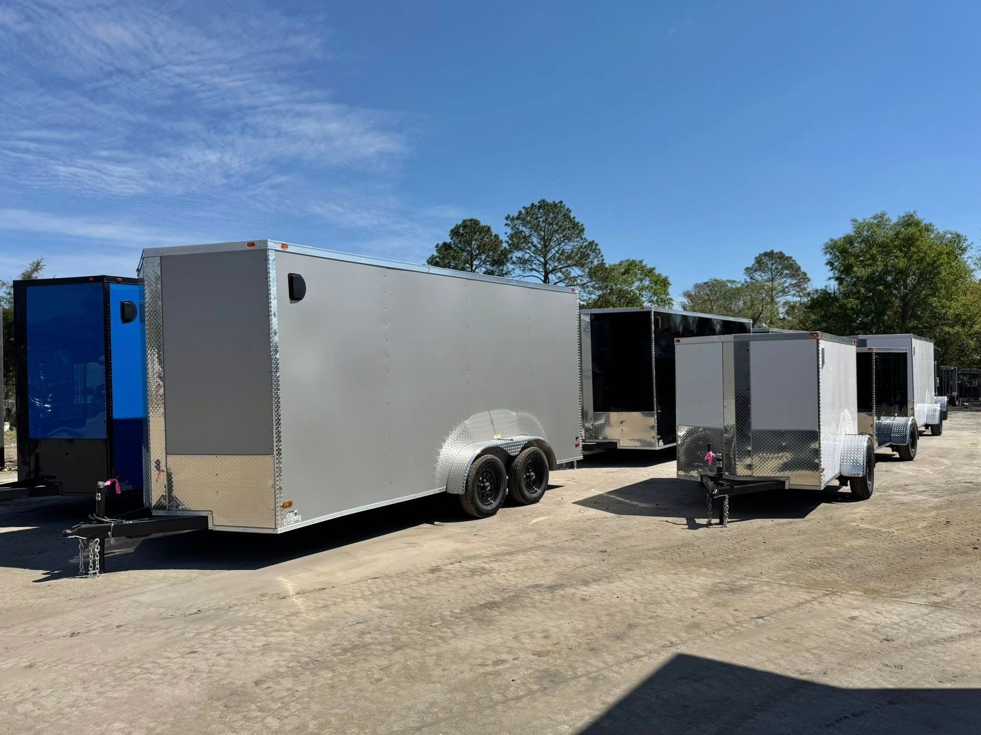 Trailers parked on gravel under a blue sky, varying colors: silver, black, and blue.