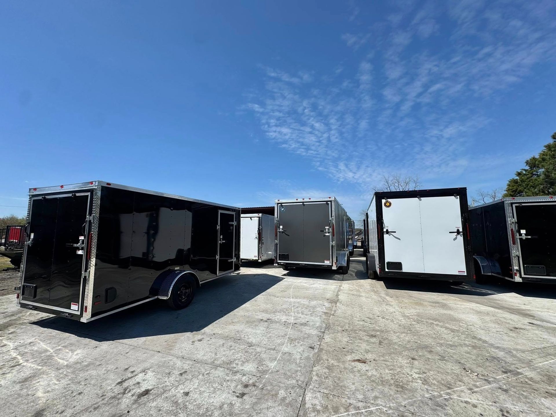 Several enclosed cargo trailers parked on a concrete surface under a blue sky.
