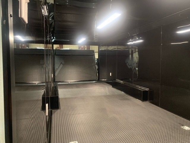 Inside a black enclosed trailer, with metal floor and overhead lights.