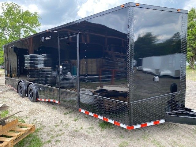 Black enclosed trailer with open door, tires inside, outdoors.