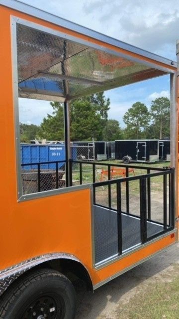 Orange food trailer with a serving window and a small deck with black railing.