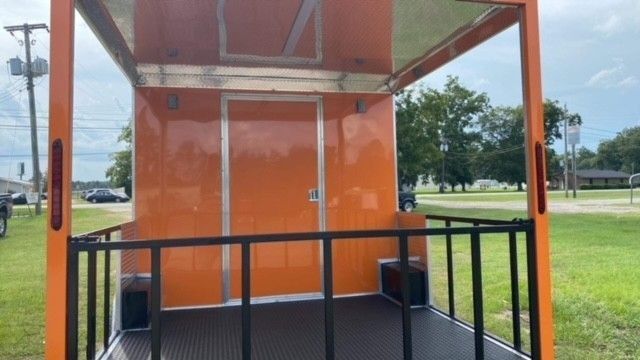 Orange enclosed trailer with black railings, door, and a black floor, parked outdoors.