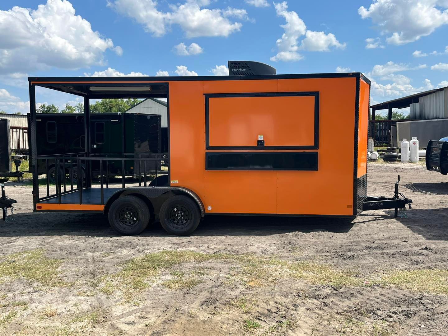 Orange food trailer with black accents, awning, and service window, parked outdoors.