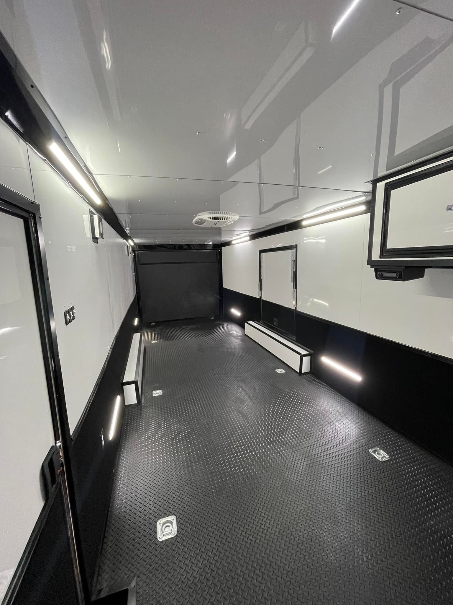 Interior view of a trailer with black and white walls and floor, lit with overhead lights.