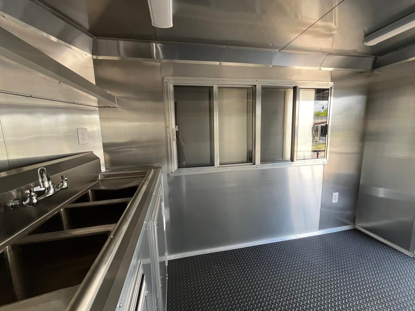 Interior of an empty food truck, featuring stainless steel walls, sinks, and a serving window.