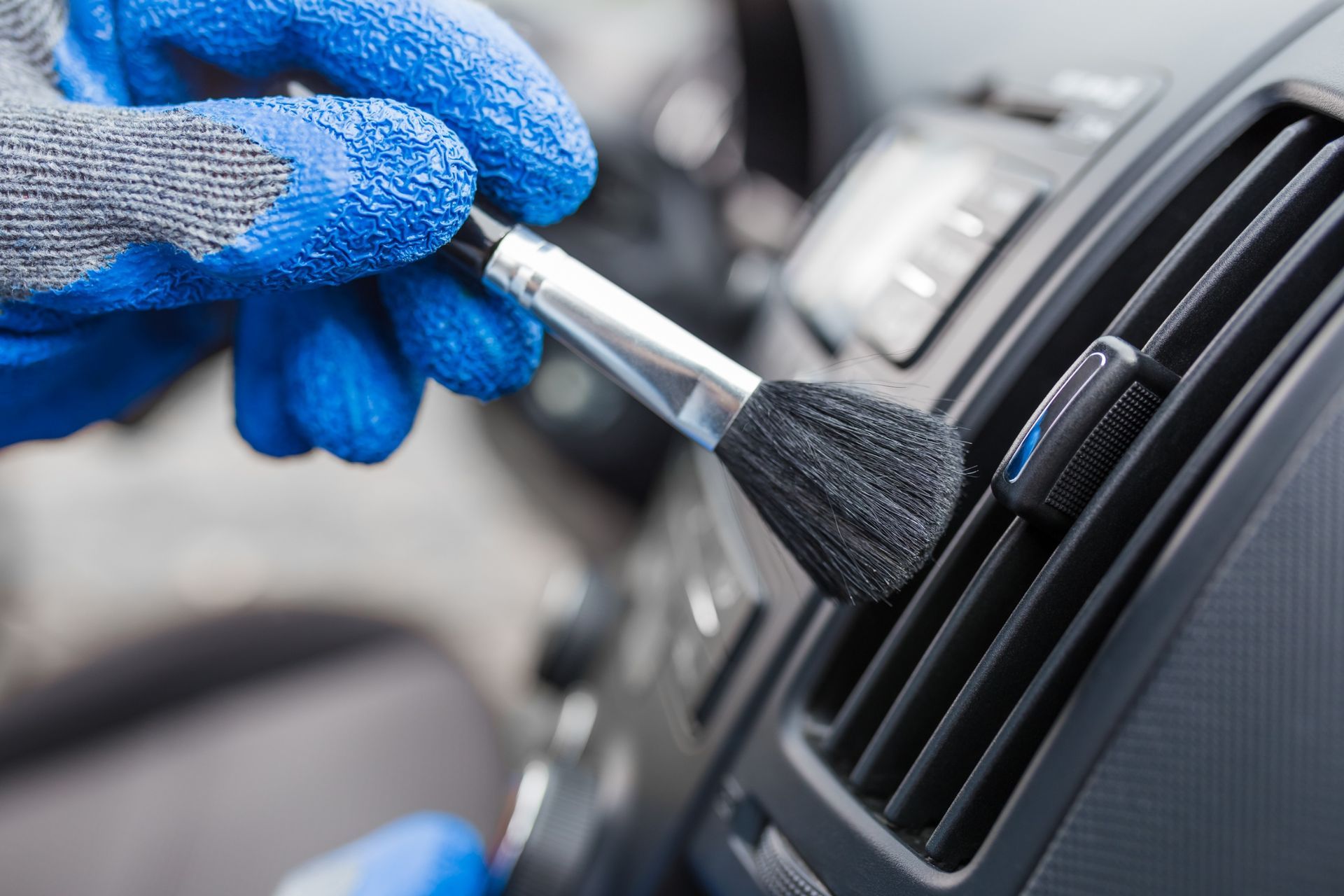 Gloved hand cleaning a car dashboard vent with a small brush