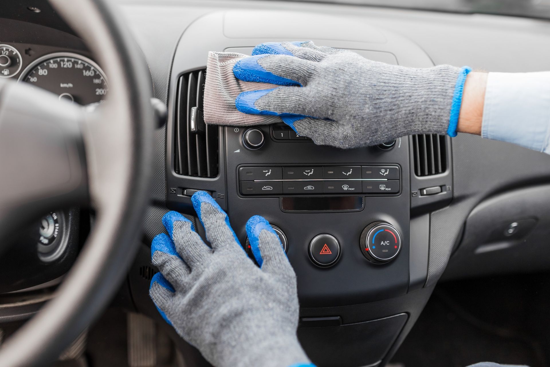 Gloved hands cleaning a car dashboard and air vents with a cloth and spray bottle