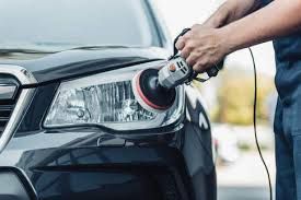 Person polishing a black car headlight with a handheld buffer at a car wash