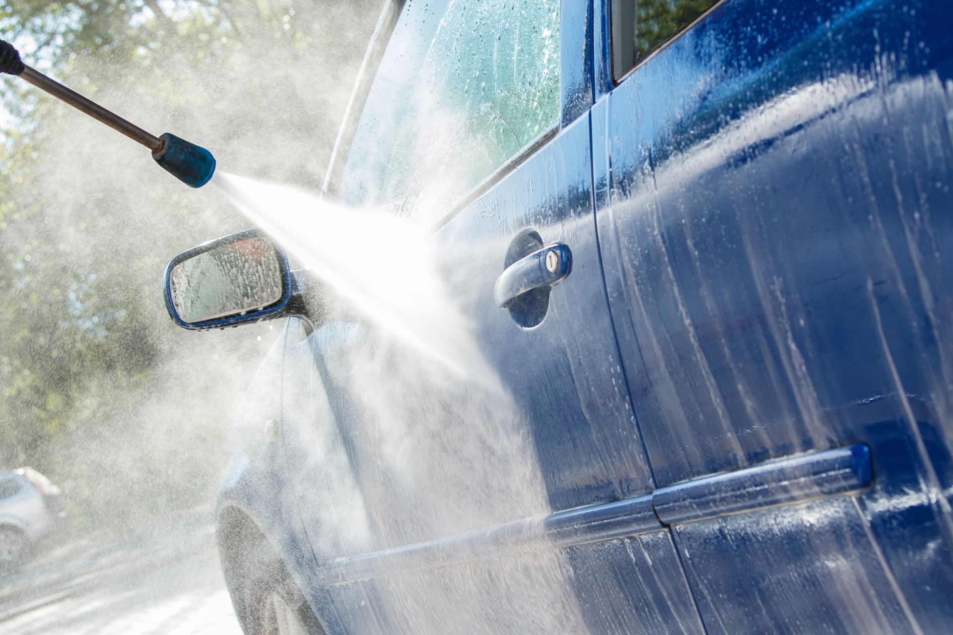 Car being pressure washed, with a strong spray of water hitting the blue door and mirror
