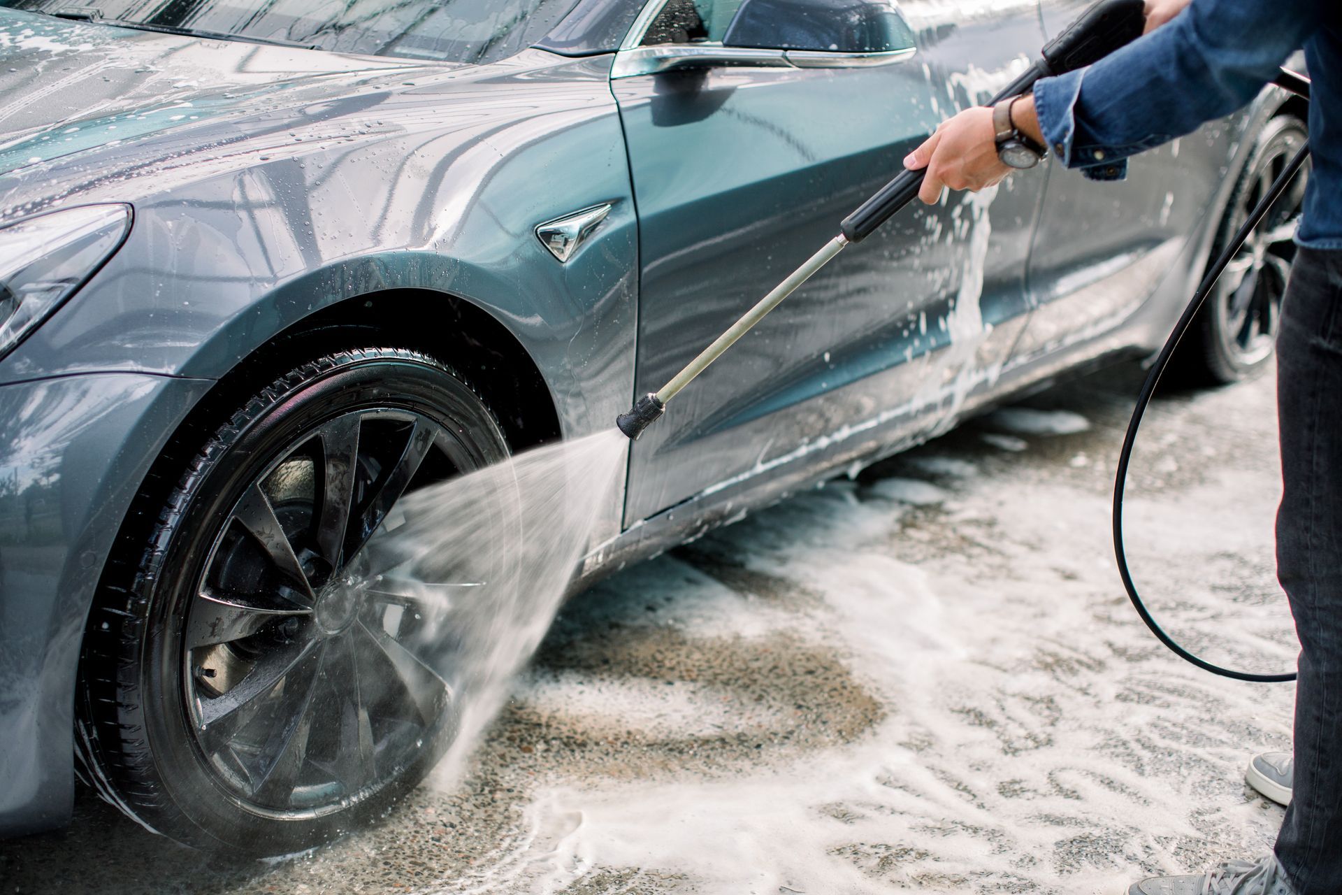 Person pressure-washing a blue car covered in soap suds