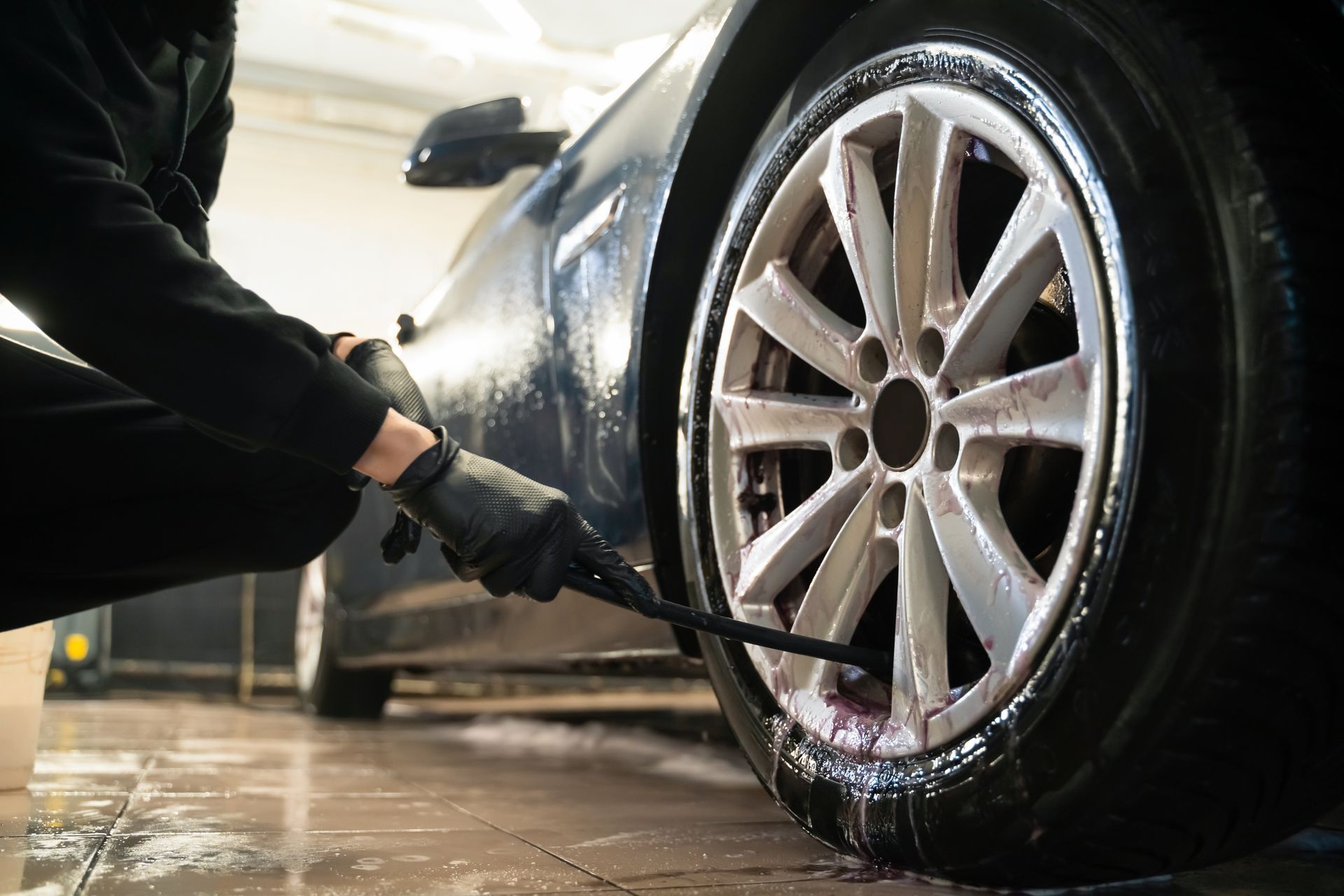 Person pressure-washing a car wheel and tire on a wet garage floor