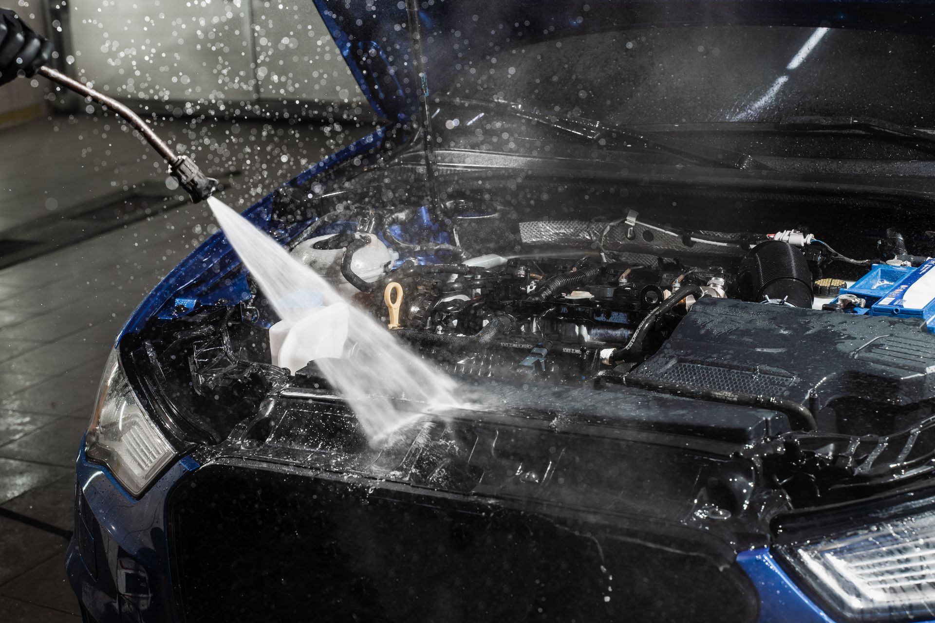 Car being pressure washed, water spraying across the open hood in a car wash.