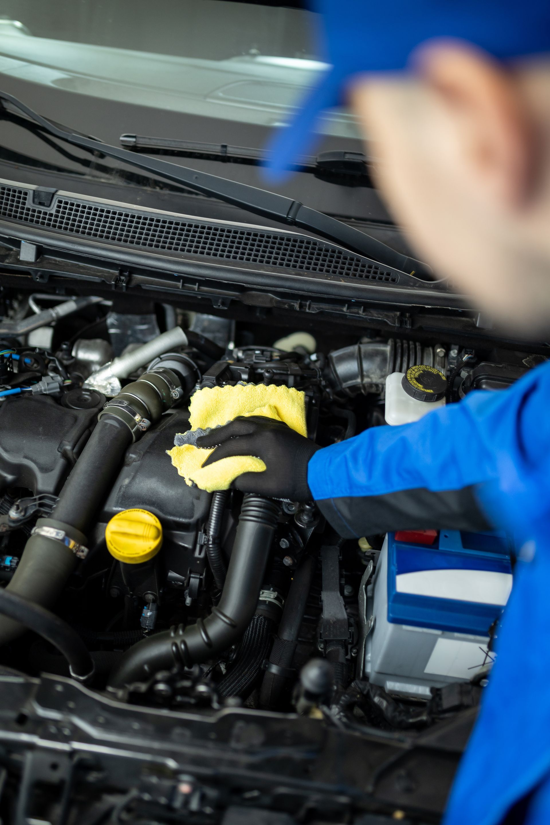 Mechanic cleaning a car engine bay with a yellow cloth and blue gloves