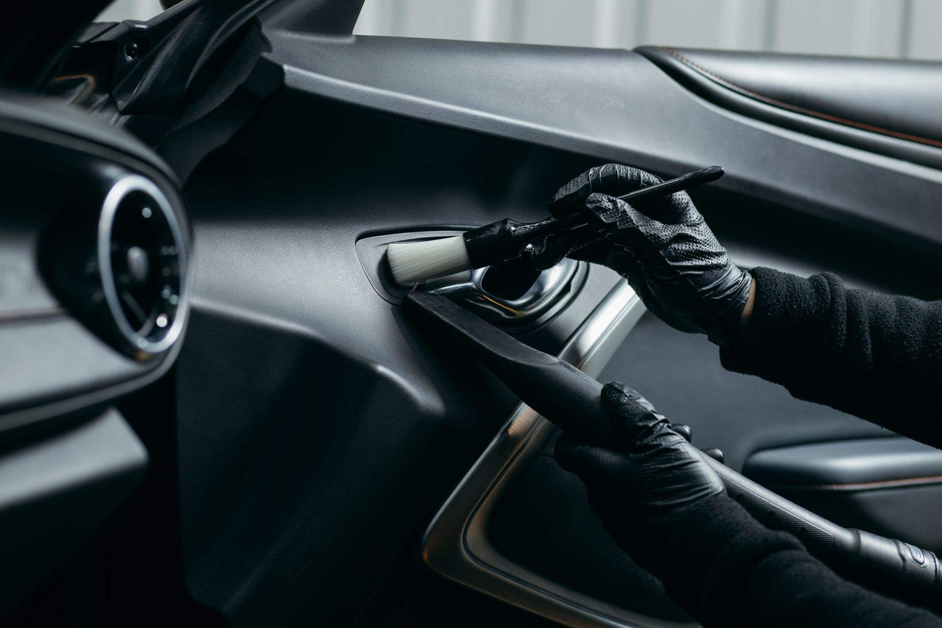 Gloved hands cleaning a car dashboard with a microfiber cloth and spray bottle