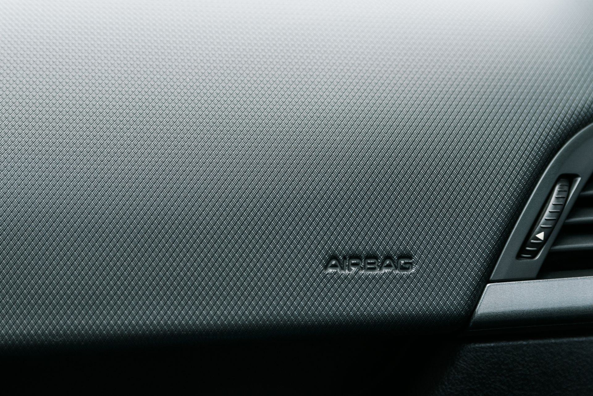 Close-up of a gray car dashboard with textured panel and a small vent on the right.