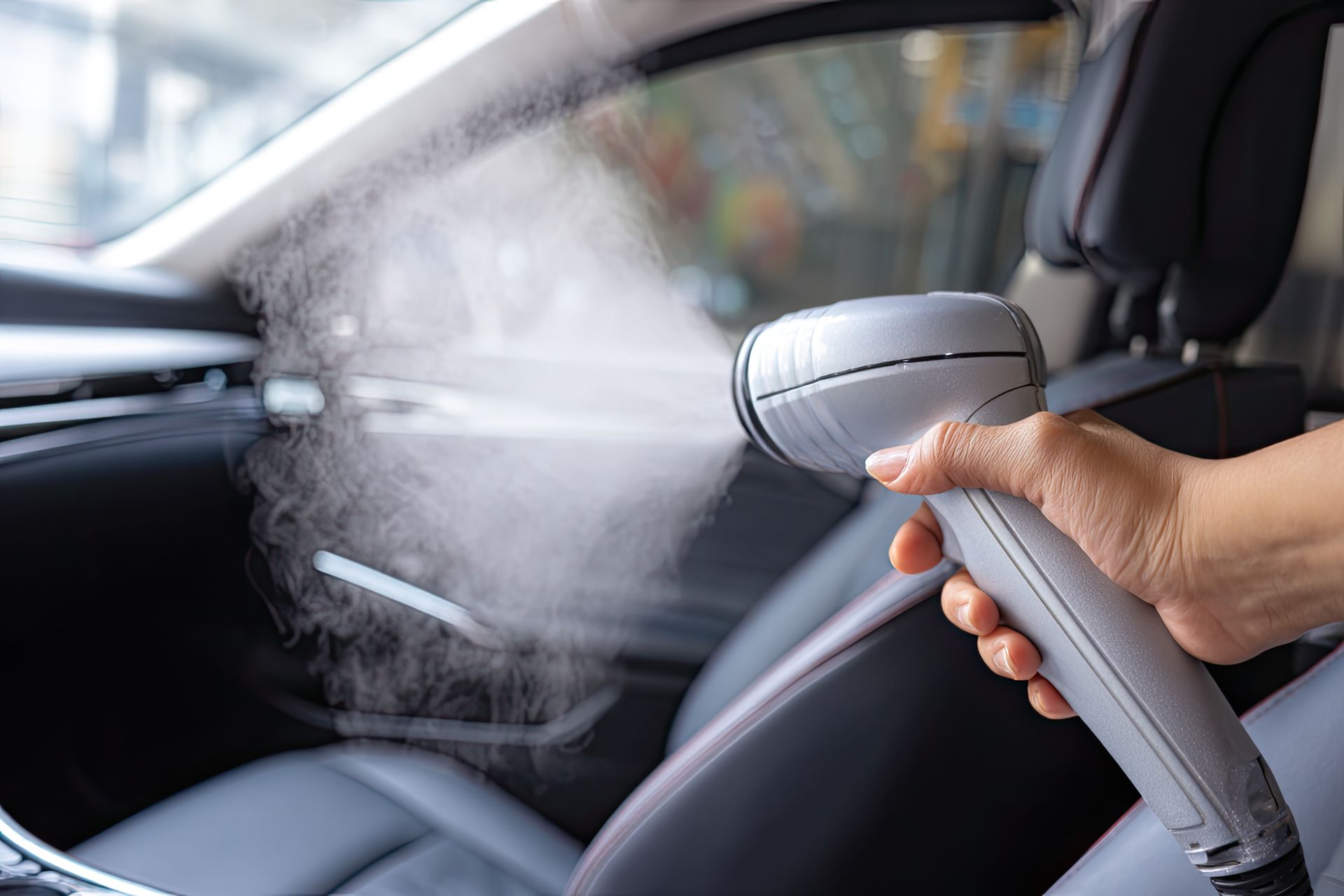 Hand spraying water onto a car dashboard interior with a cleaning brush