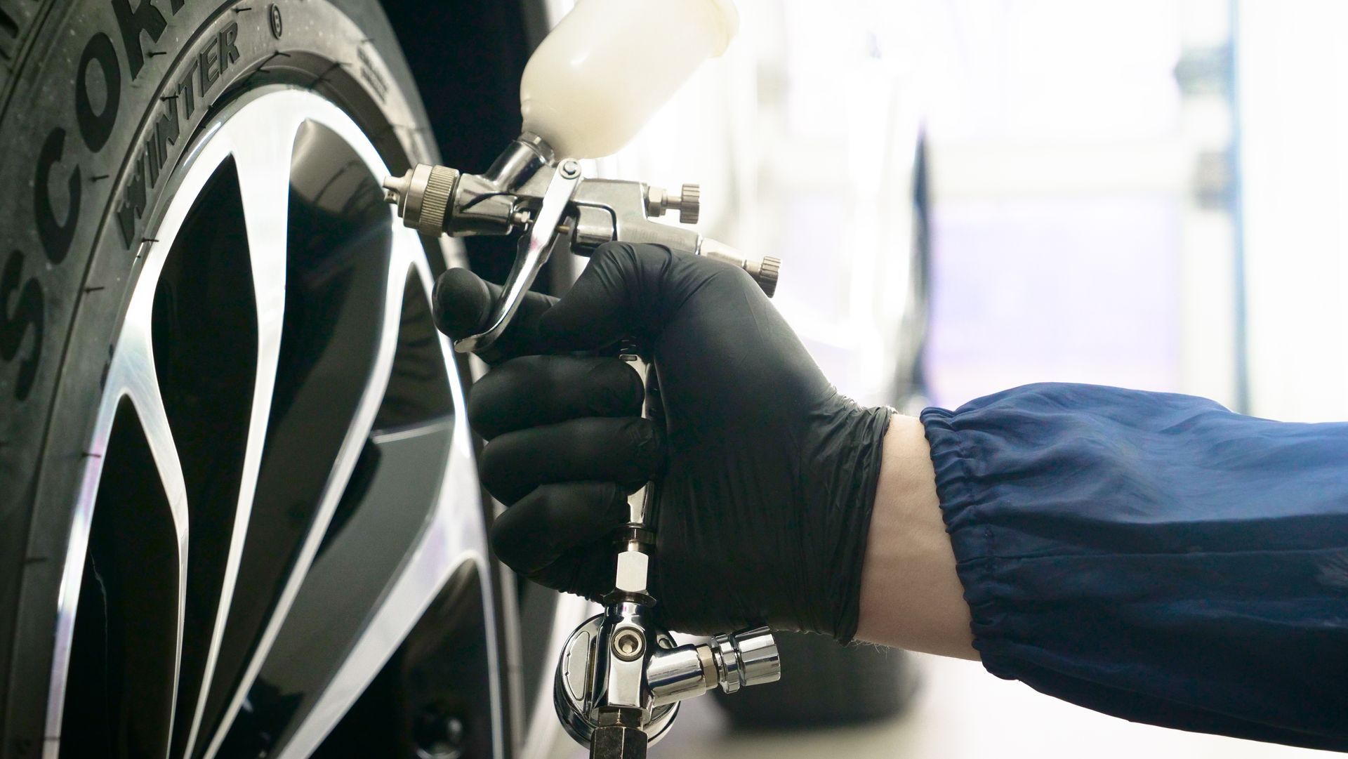 Gloved hand using an air hose to inflate a car tire on a black alloy wheel