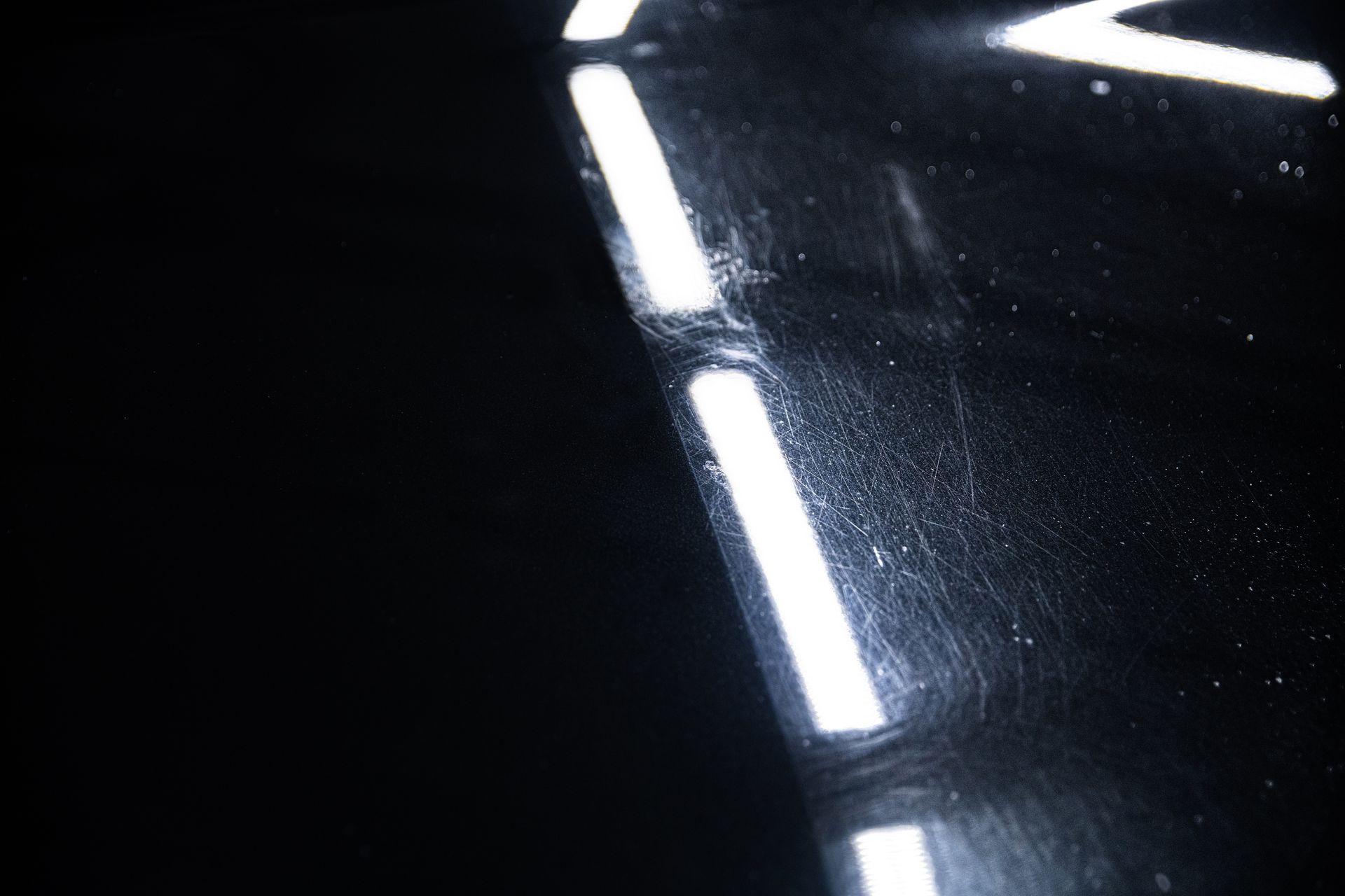Bright white light strips reflecting on a dark glossy surface, forming angular lines.