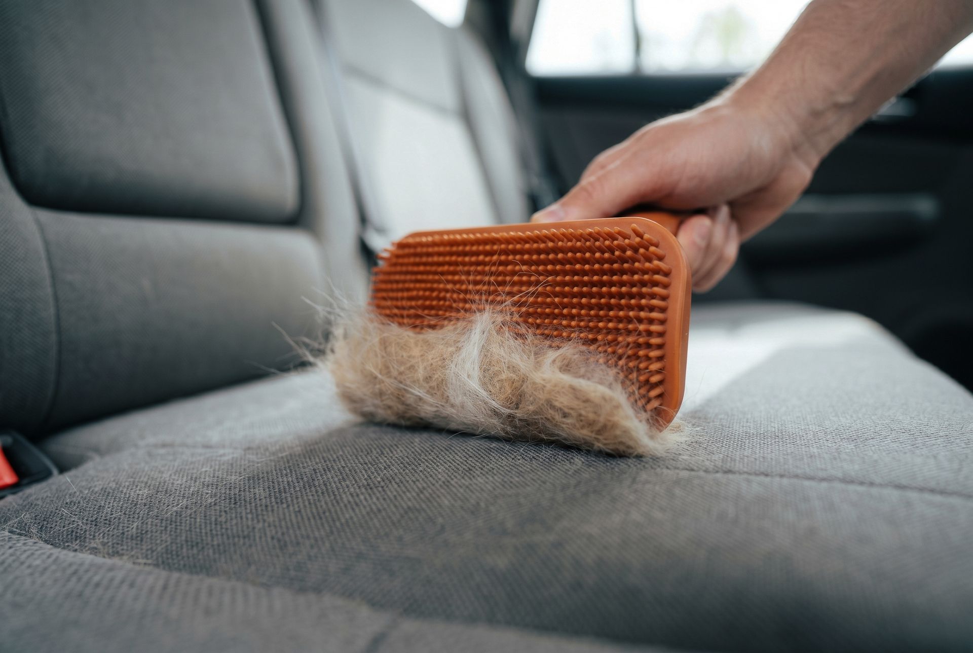 Hand brushing pet hair from a gray car seat with an orange lint brush