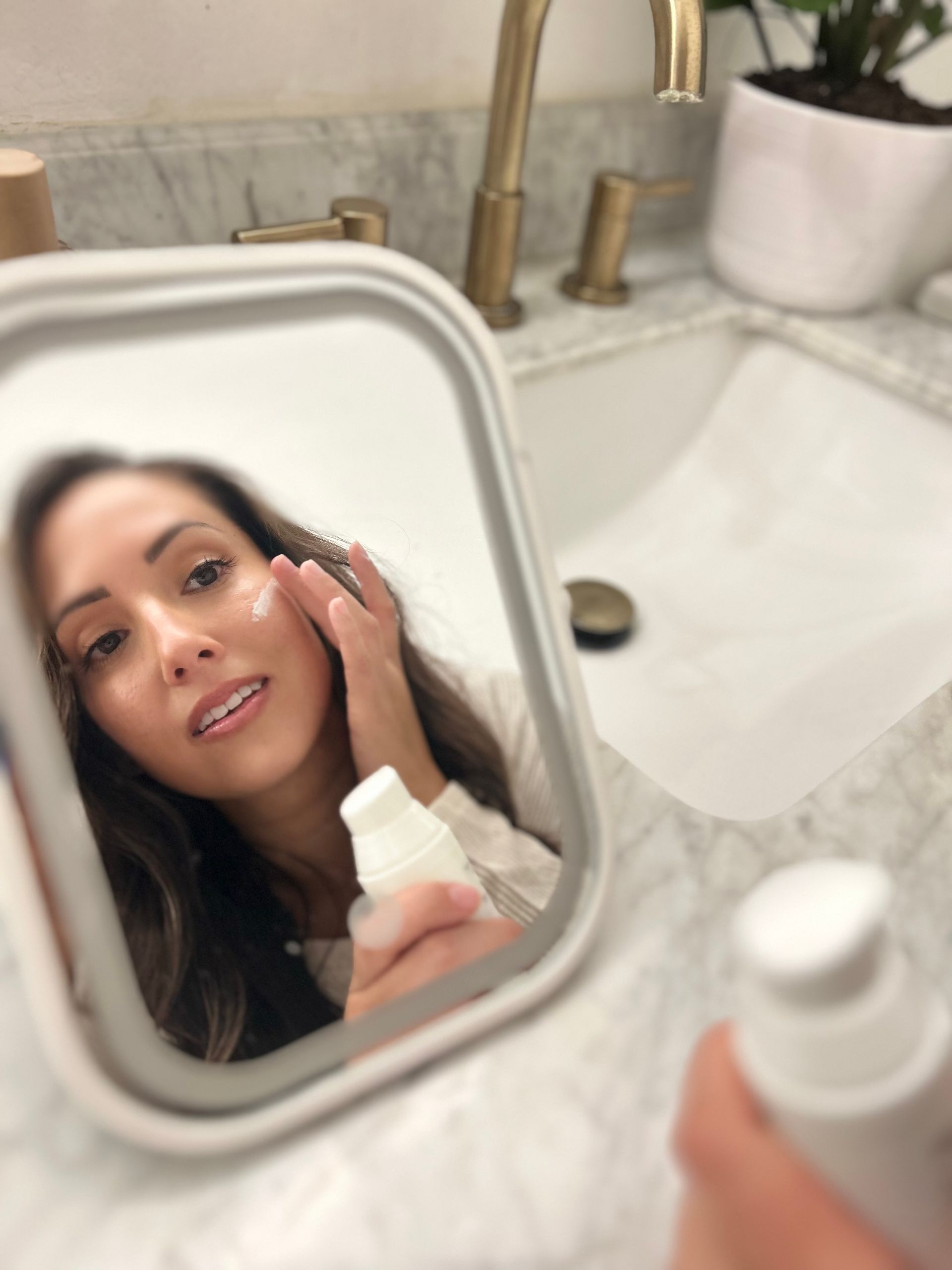 Woman applying serum to face with dropper, wearing a headband, in a bathroom.