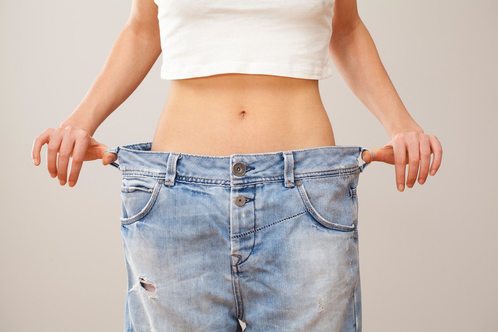 Woman in too-big jeans holding out waist, showing weight loss.