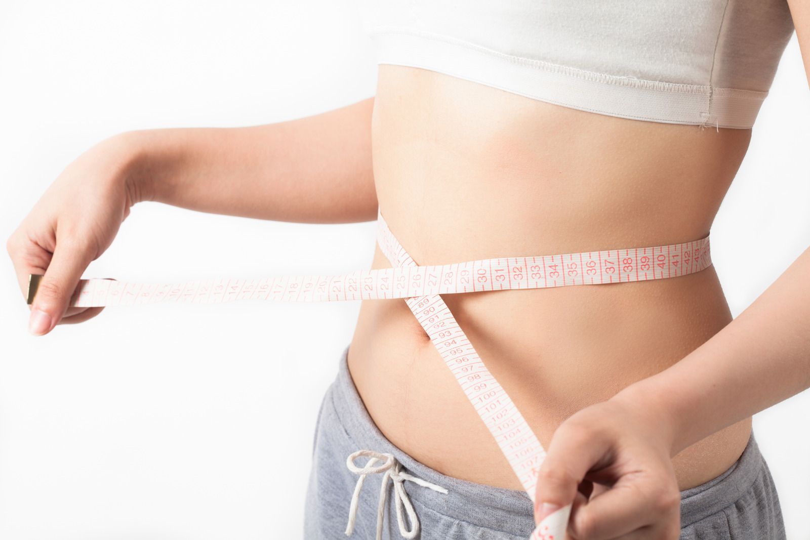 Woman measuring waist with pink measuring tape against a white background.