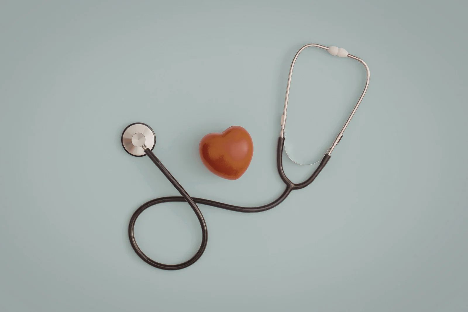 A stethoscope resting on a blue surface, next to a brown heart model.