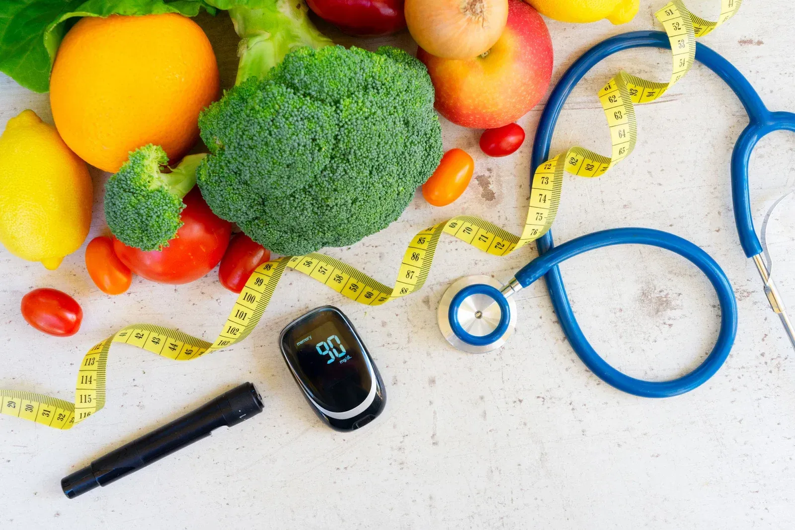 Healthy eating concept: broccoli, fruit, stethoscope, glucose meter, and measuring tape on a table.