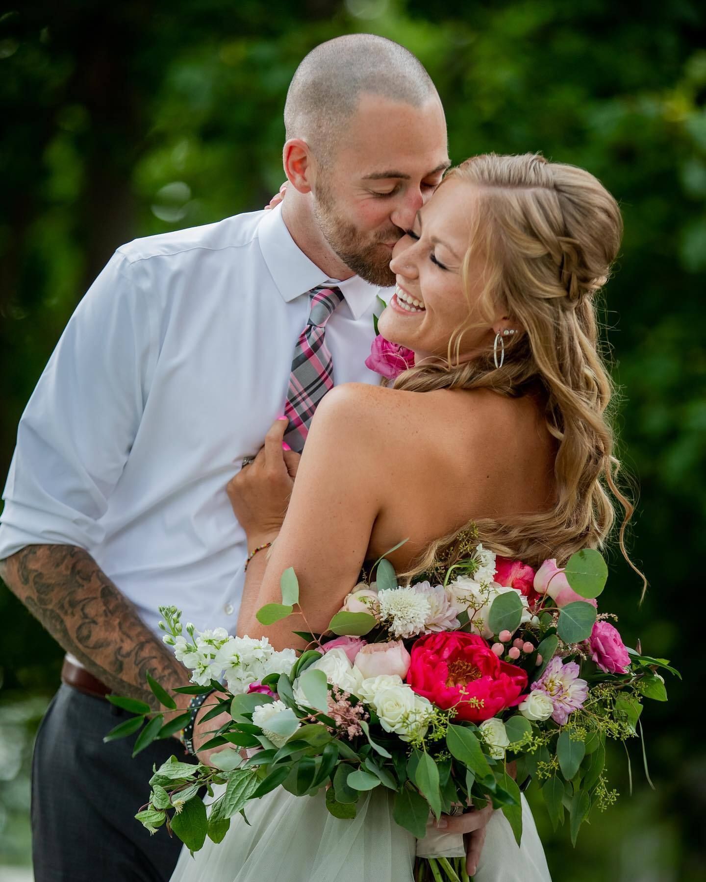 A bride and groom are kissing while the bride is holding a bouquet of flowers.