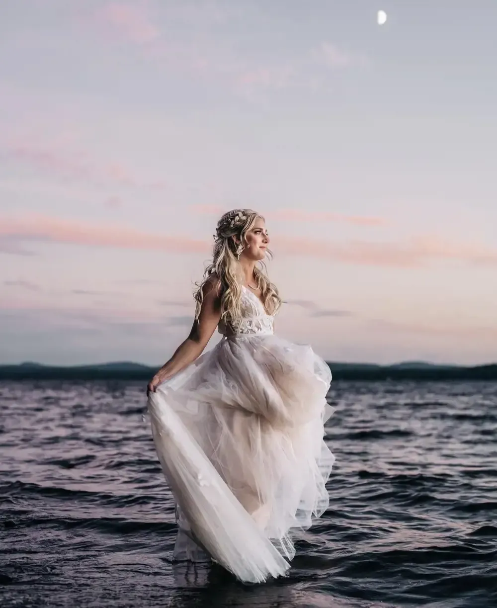 A woman in a wedding dress is standing in the water.