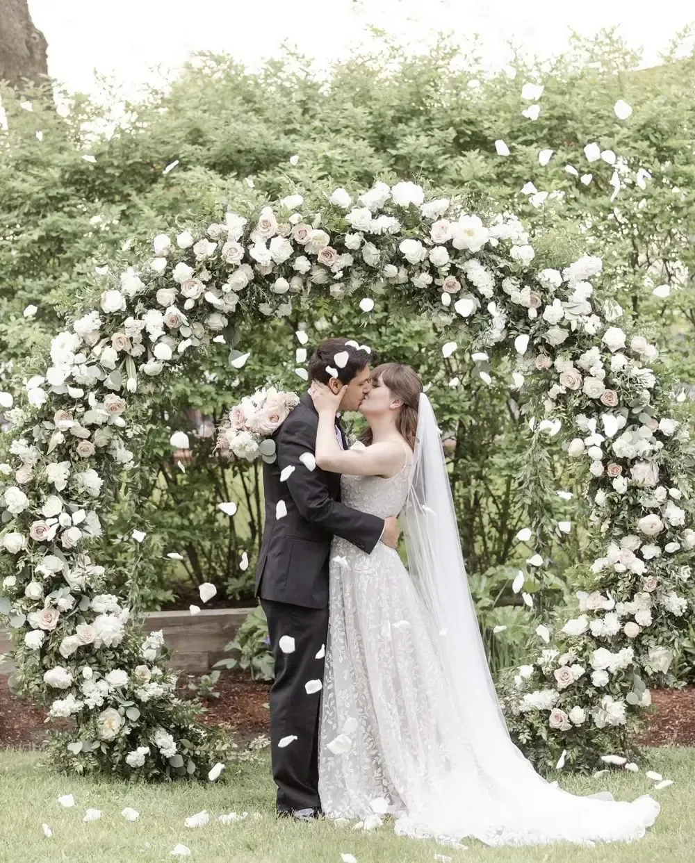 A bride and groom are kissing under a floral arch.