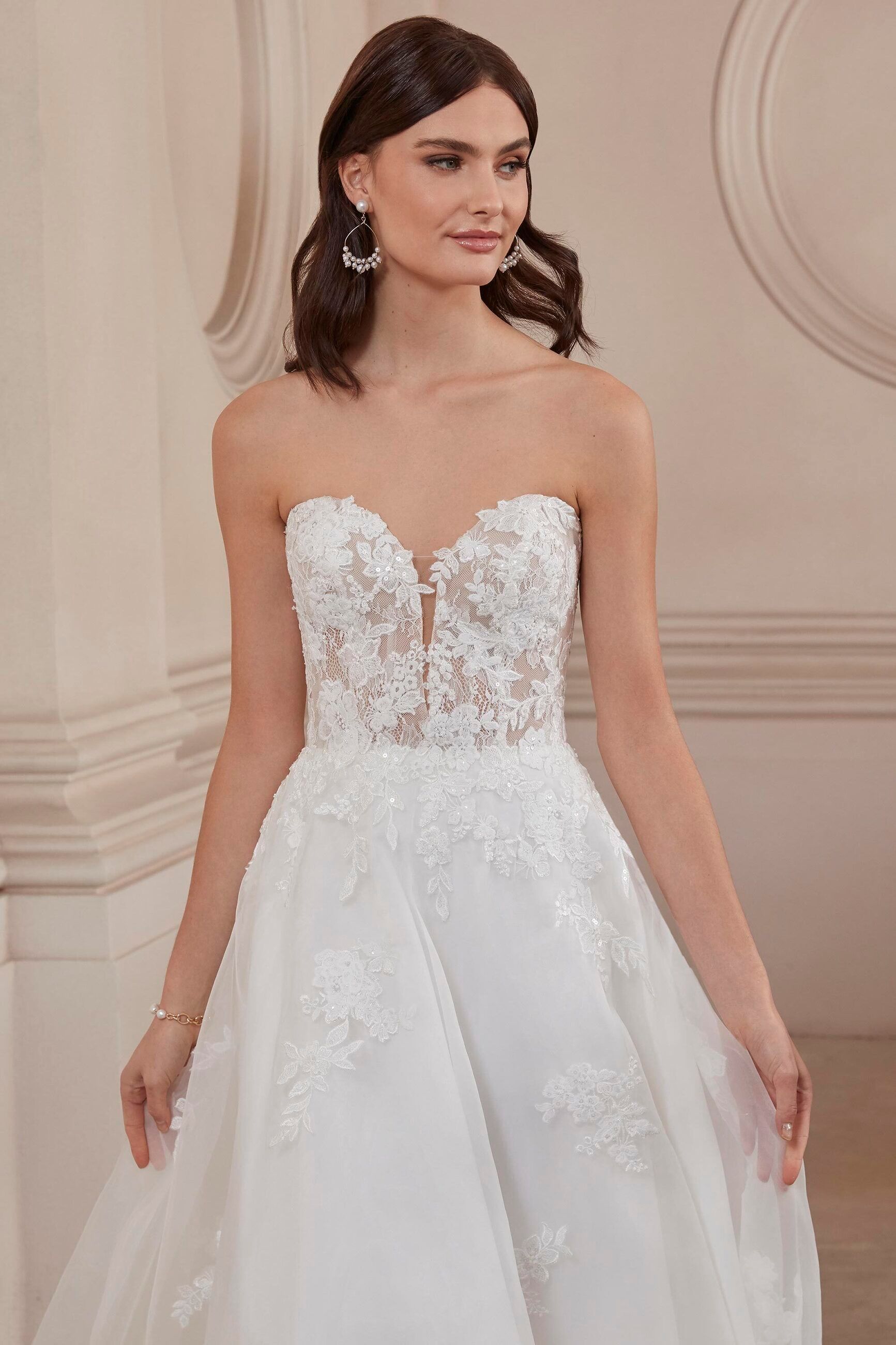 A woman in a white wedding dress is standing in front of a wall.