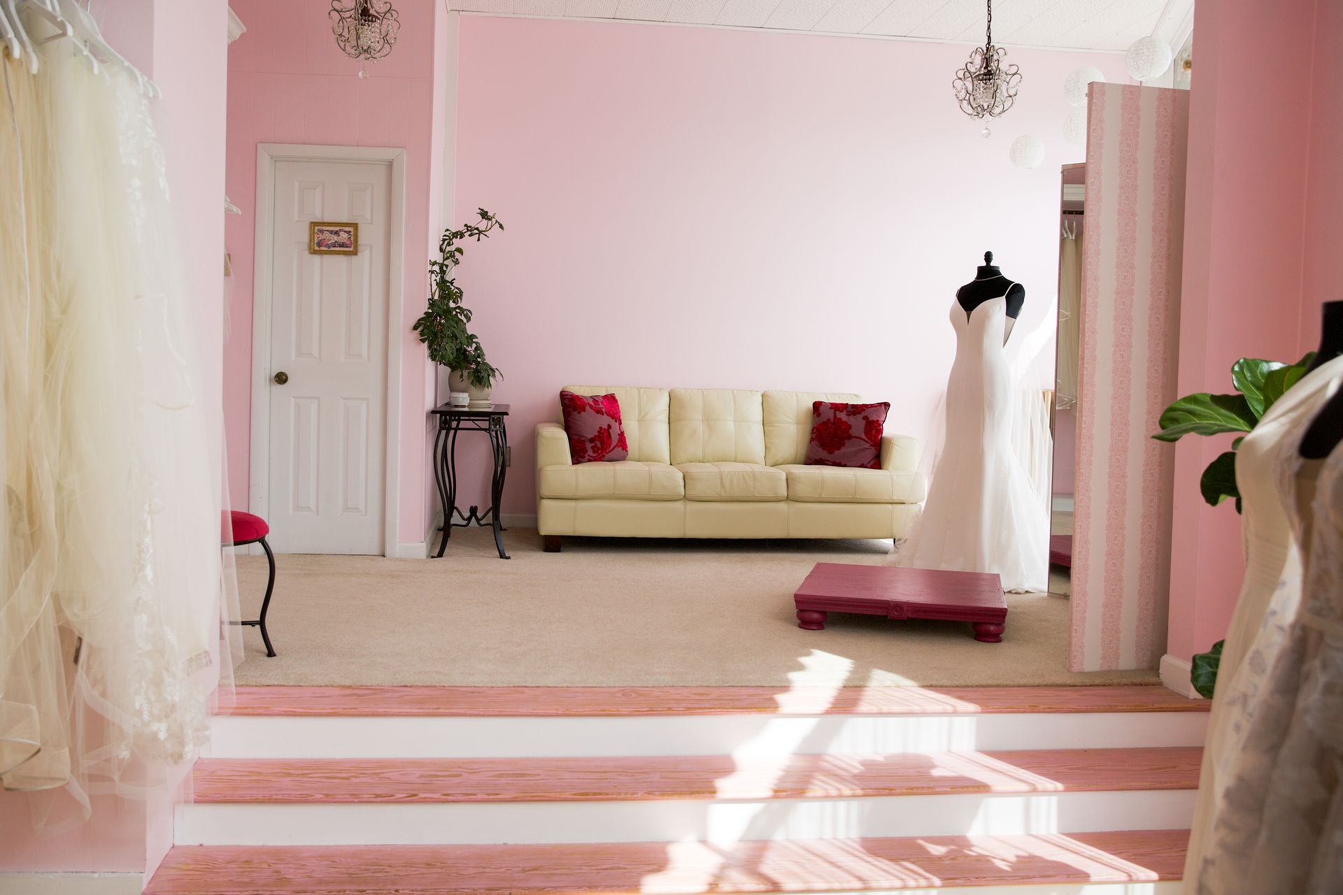 A living room with pink walls and a white couch and a white dress on a mannequin.