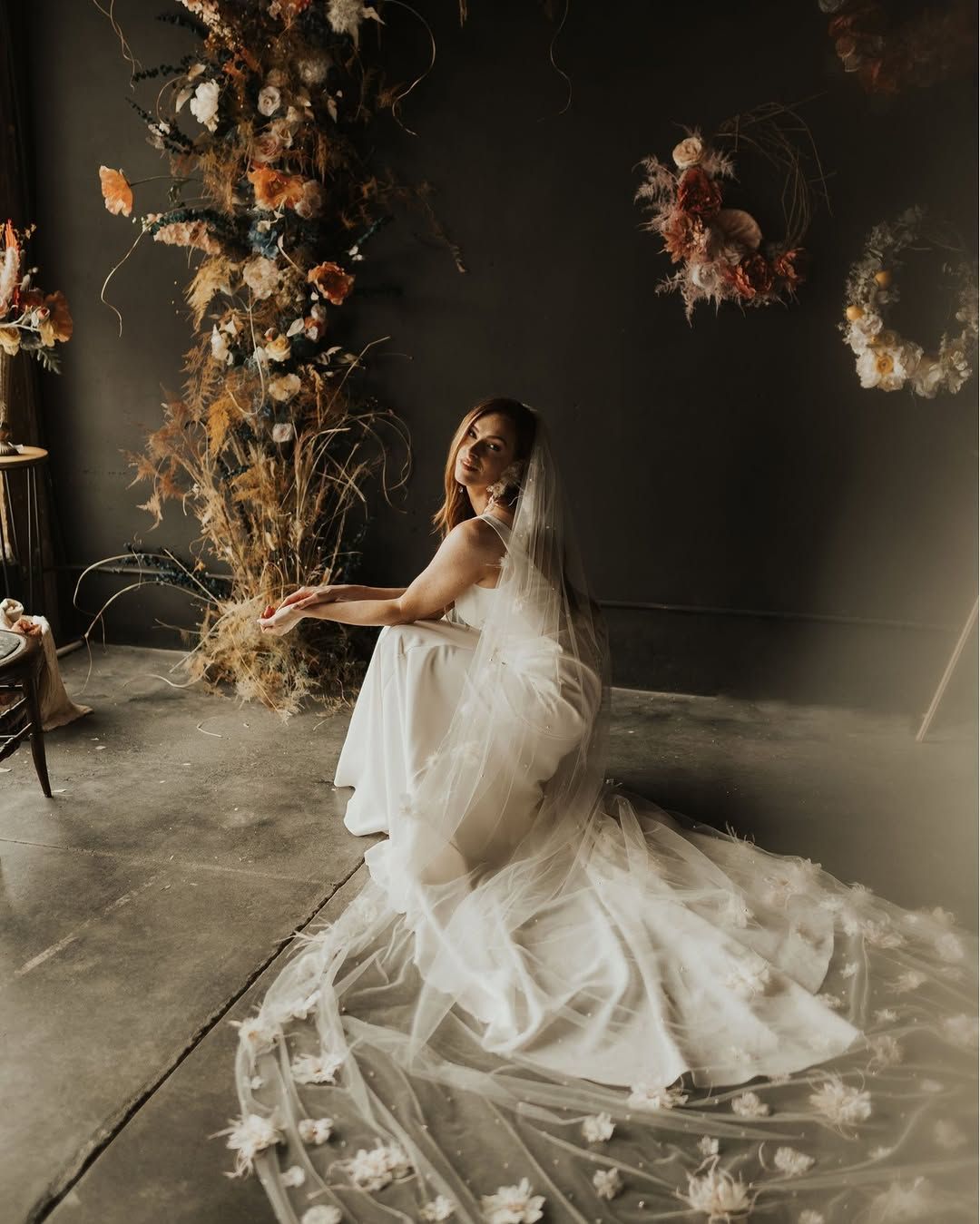 A bride in a wedding dress and veil is sitting on the floor.