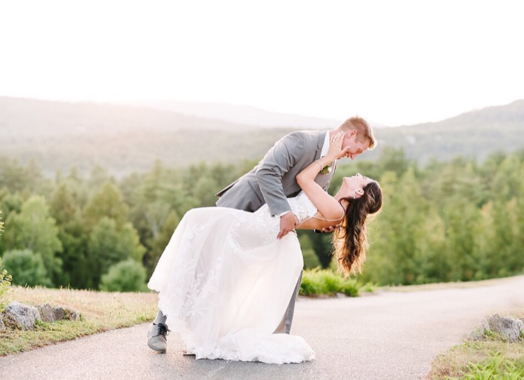 A bride and groom are posing for a picture while the bride is being lifted in the air by the groom.