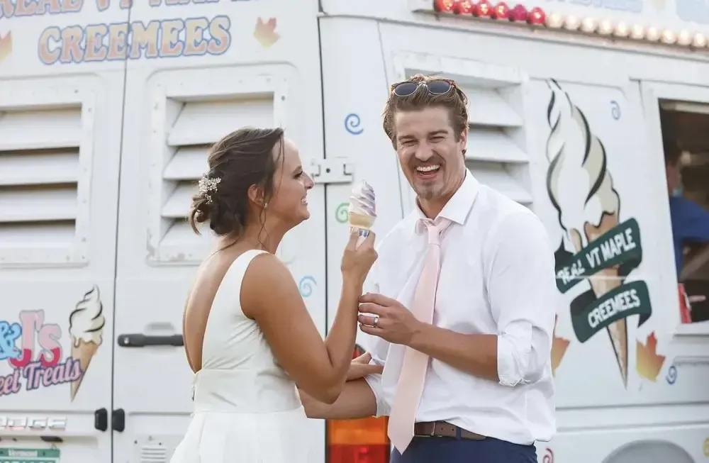 A bride and groom are standing in front of an ice cream truck.