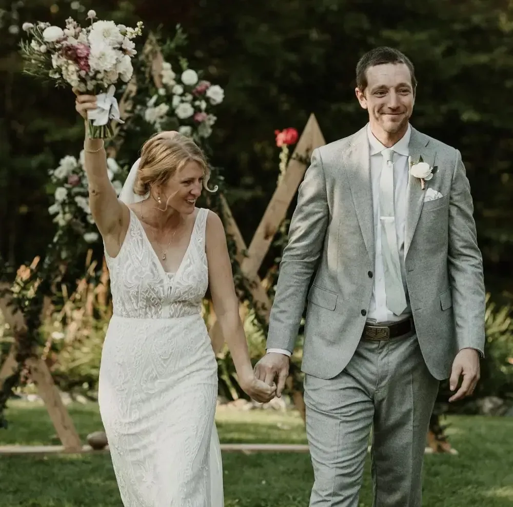 A bride and groom are walking down the aisle holding hands and the bride is holding a bouquet of flowers.