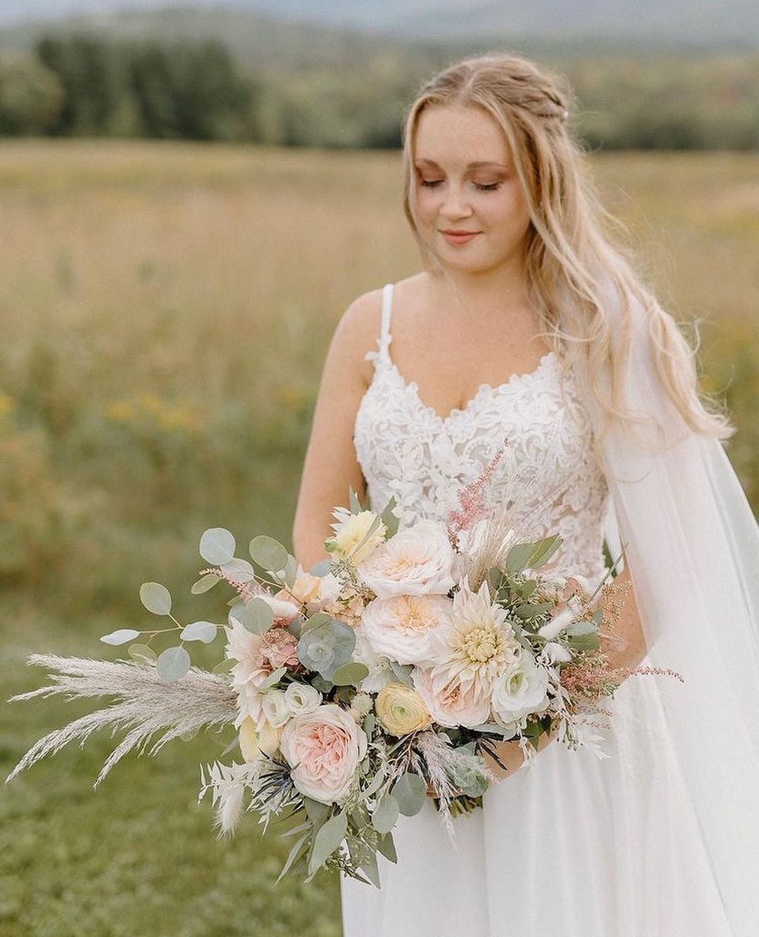 A bride in a wedding dress is holding a bouquet of flowers in a field.