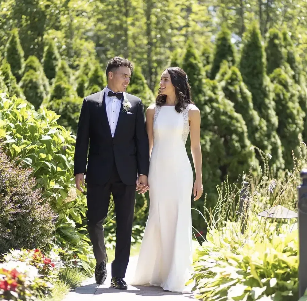 A bride and groom are walking down a path holding hands