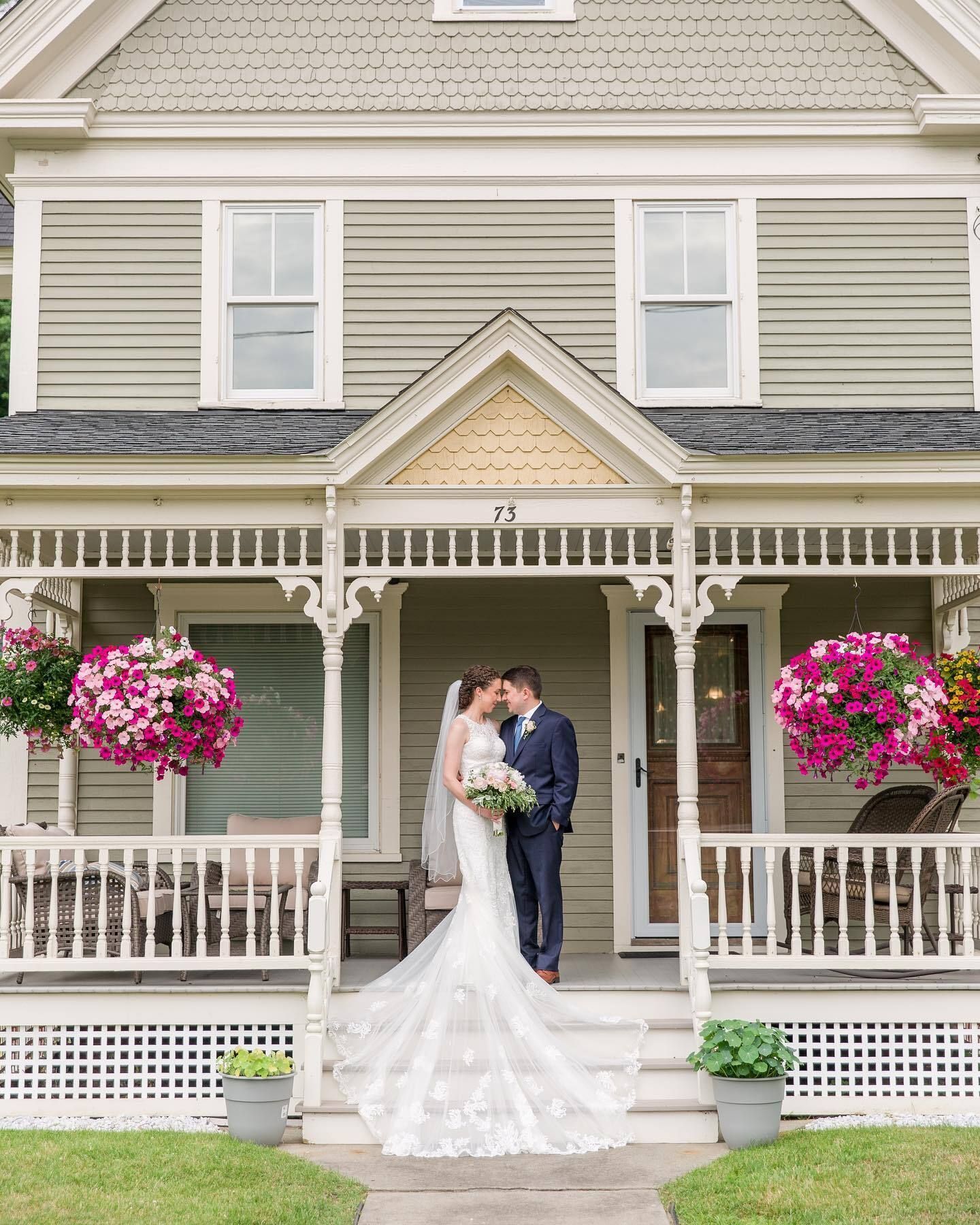 A bride and groom are kissing on the porch of a house.