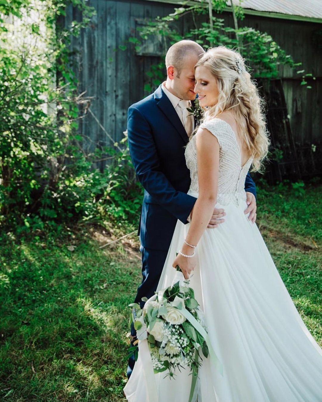 A bride and groom are posing for a picture in front of a barn.